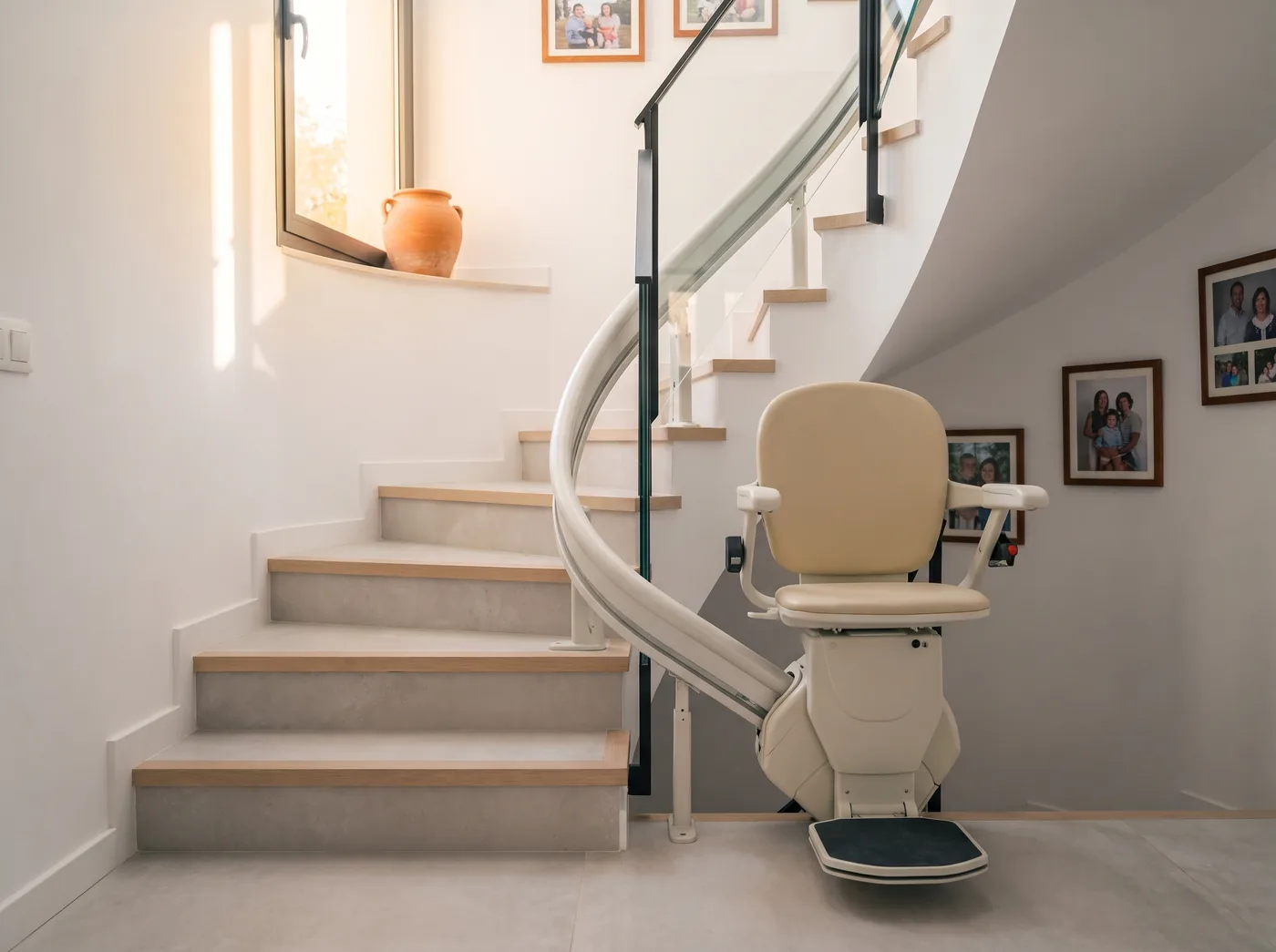 Silla salvaescaleras aparcada al pie de una escalera curva, con el raíl pegado al lado interior (imagen generada con IA)